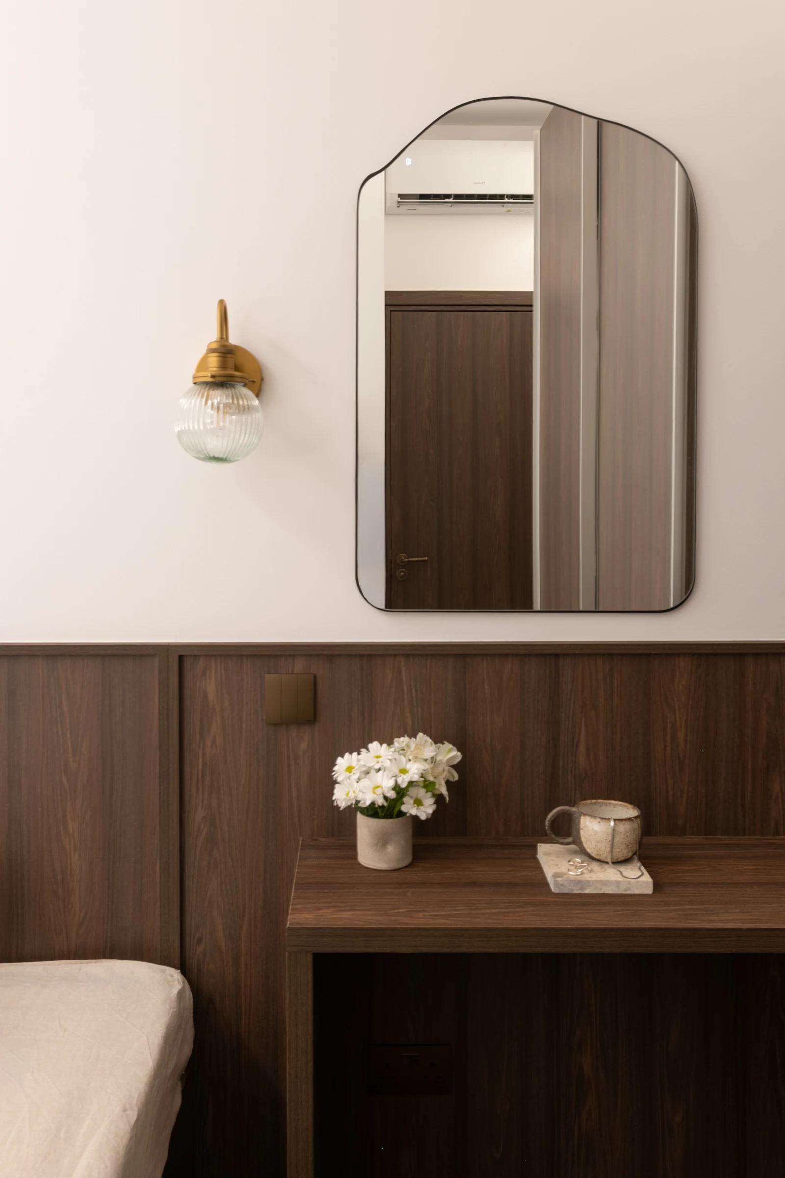 A small timber bedside table beneath an arched mirror and a glass pendant light.