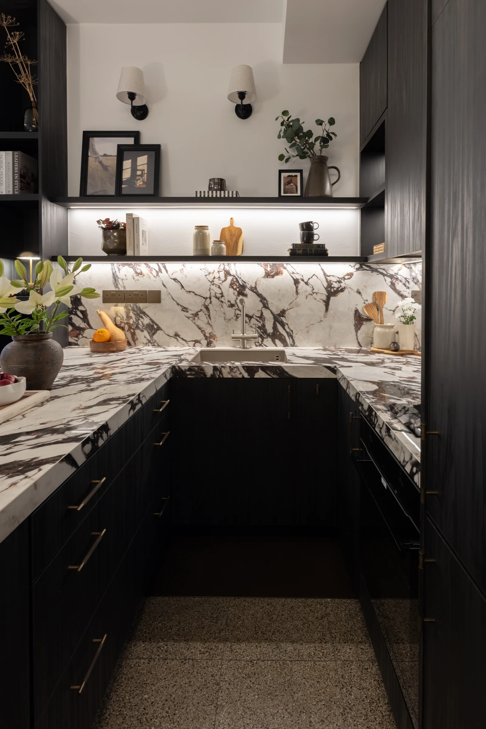 Dark kitchen cabinetry with pale veined worktops and an illuminated splashback.