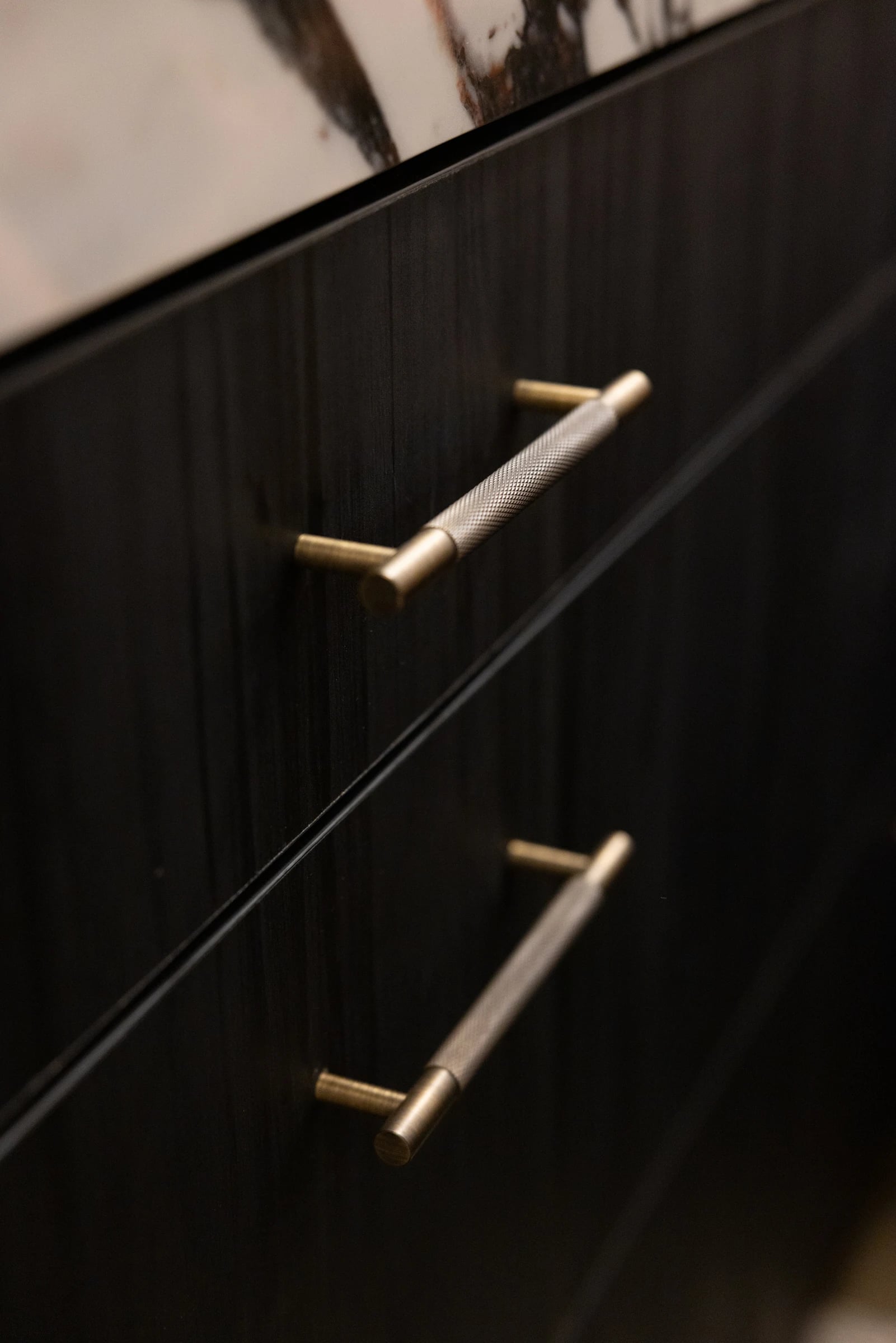 Close view of brass-coloured handles on dark timber cabinet fronts.
