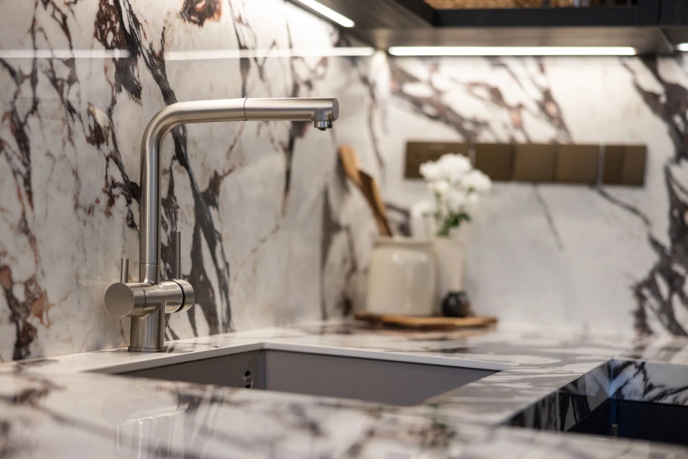 Close view of a kitchen sink and curved tap against a veined stone-patterned splashback.