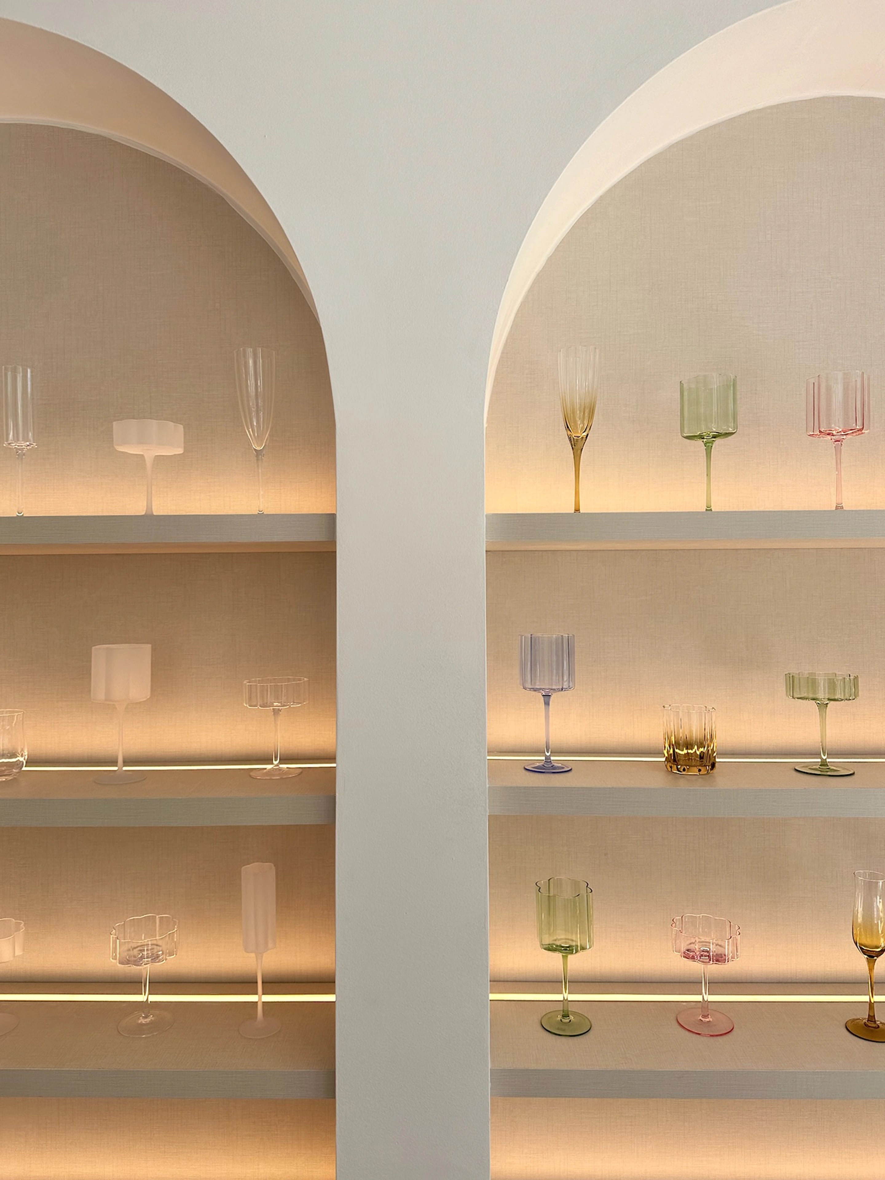 Two curved display alcoves with softly lit shelves of coloured glassware.