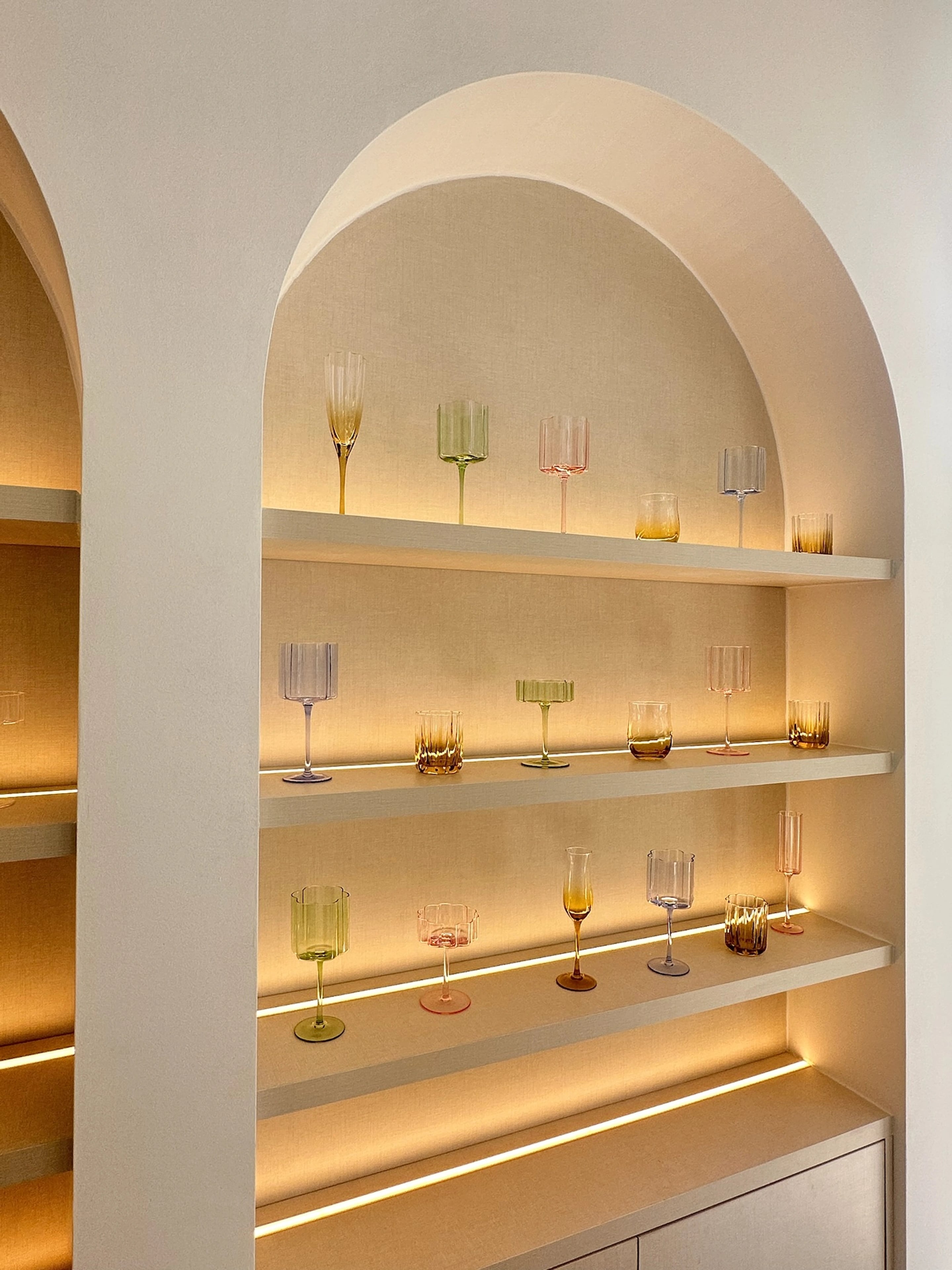 Coloured stemmed glasses displayed on illuminated shelves within a rounded arch.
