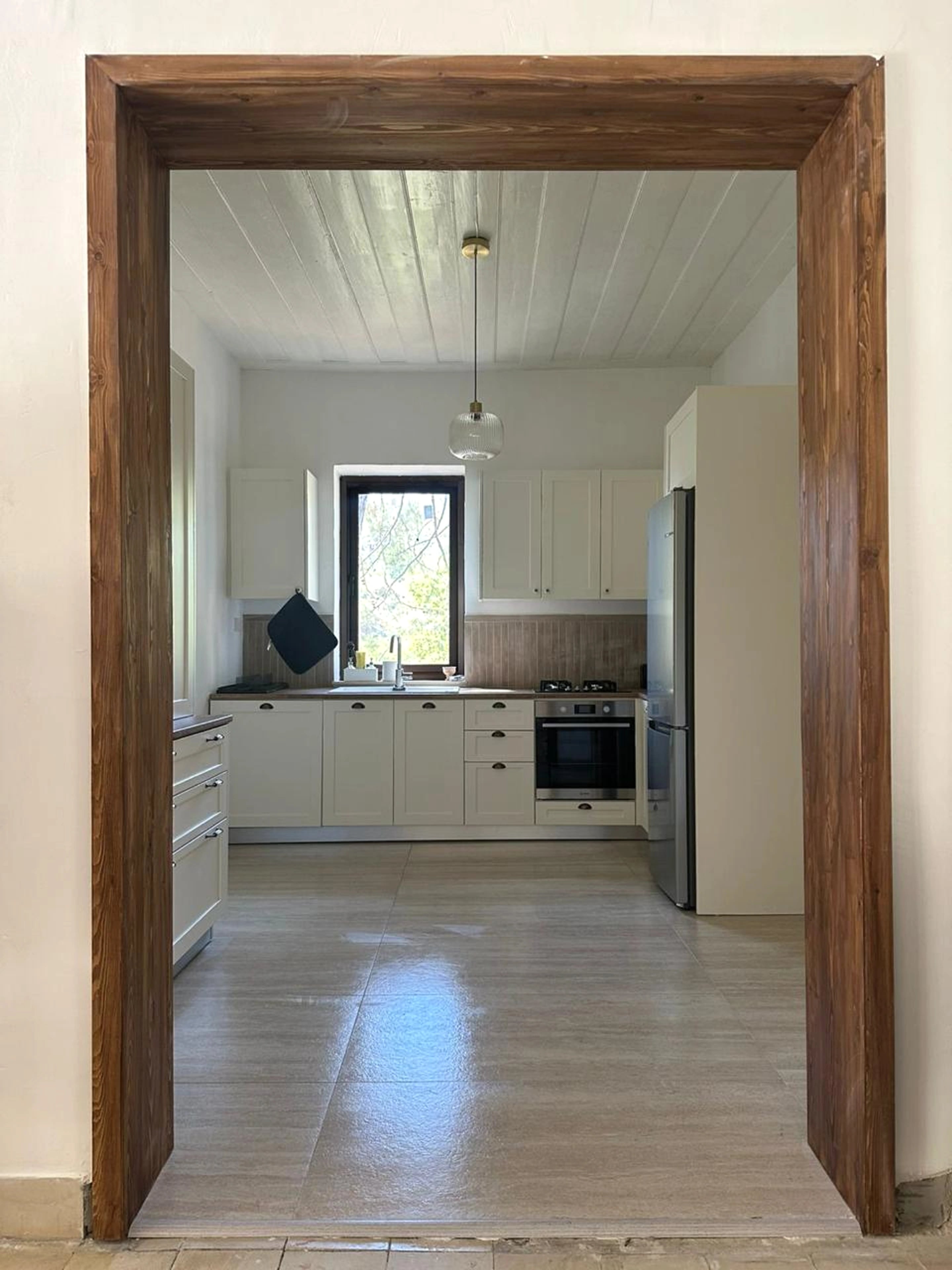 A timber-framed doorway opening toward a pale kitchen beneath a white timber ceiling.