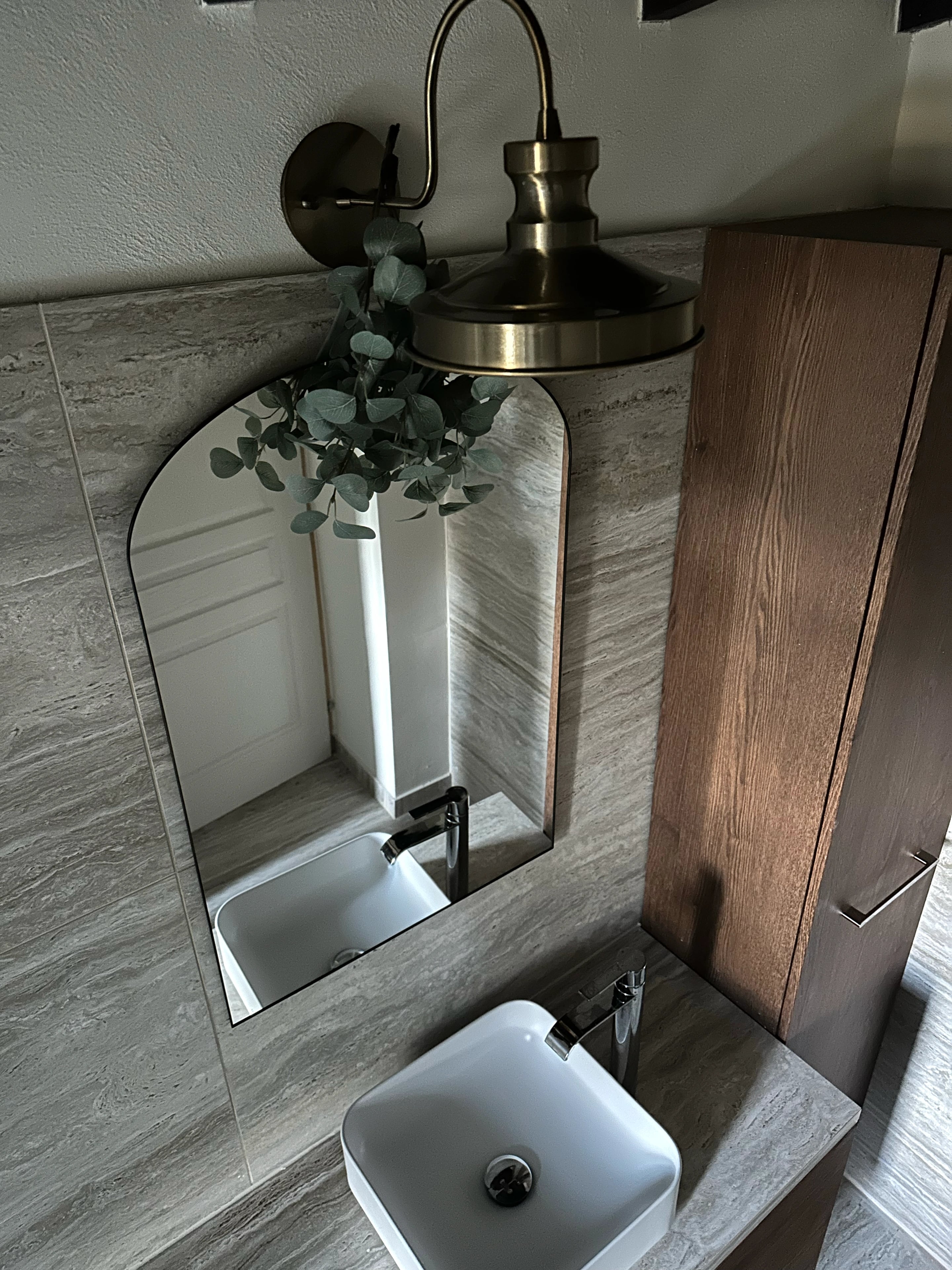A square white basin on a timber vanity beneath an arched mirror and a pendant light.