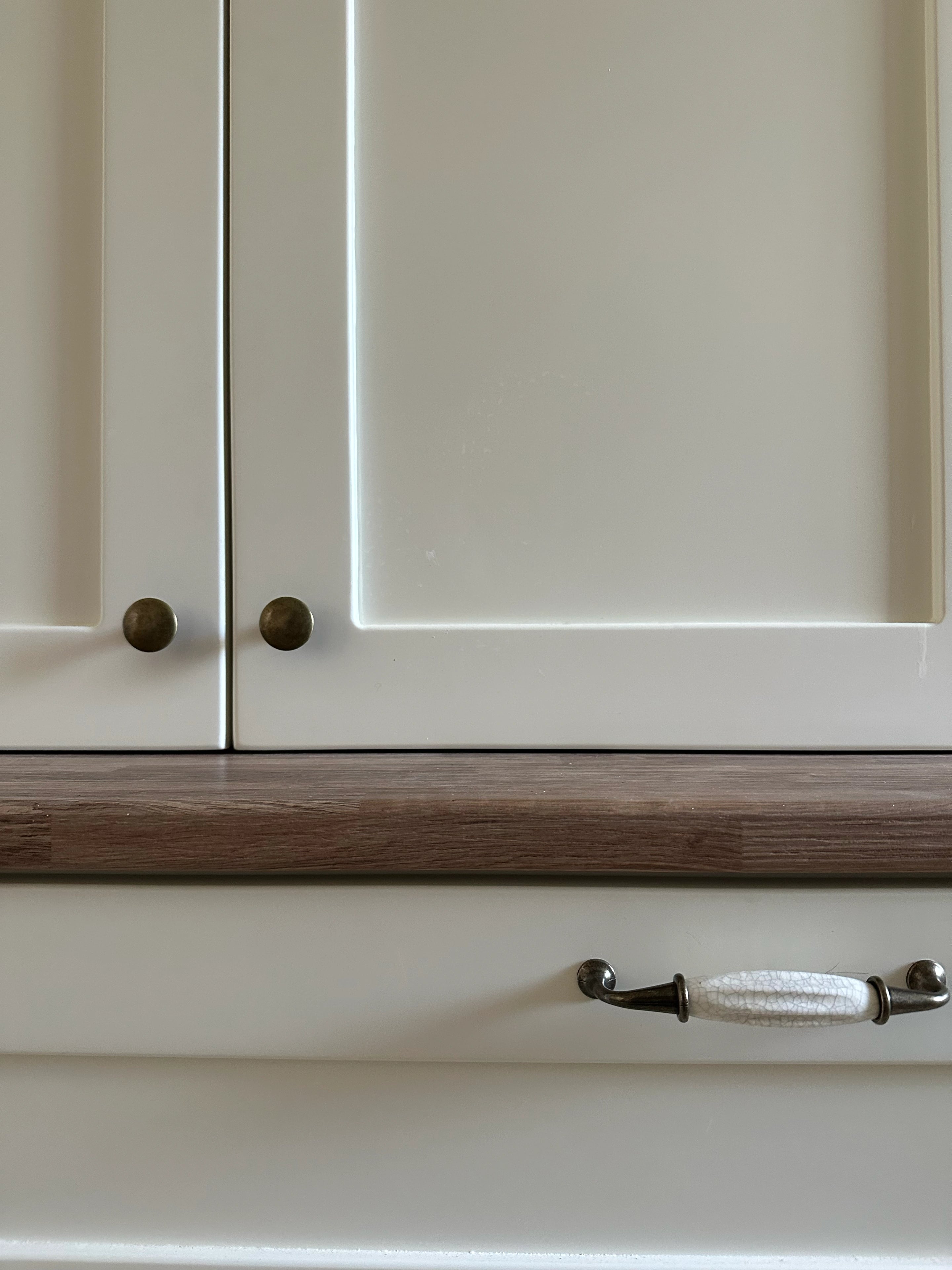Close view of cream cabinet fronts, round knobs and a timber worktop.