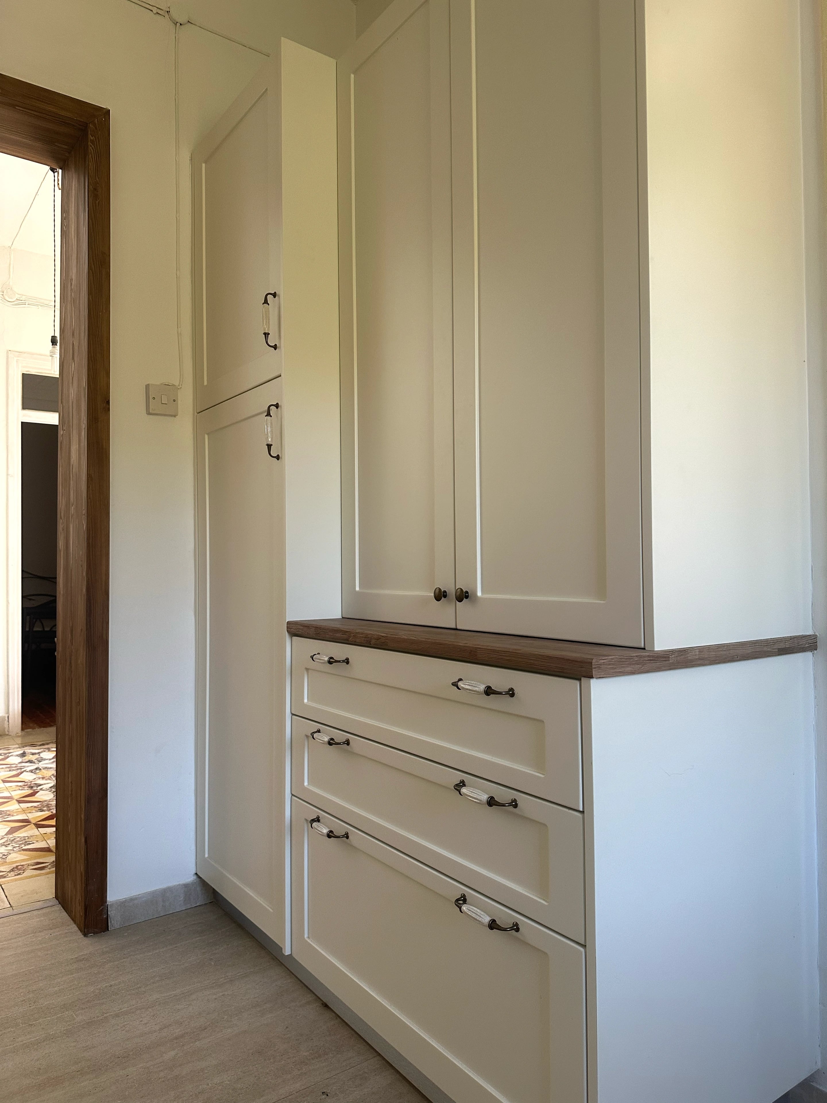Cream fitted kitchen cabinets with timber worktops beside an exposed timber doorway.