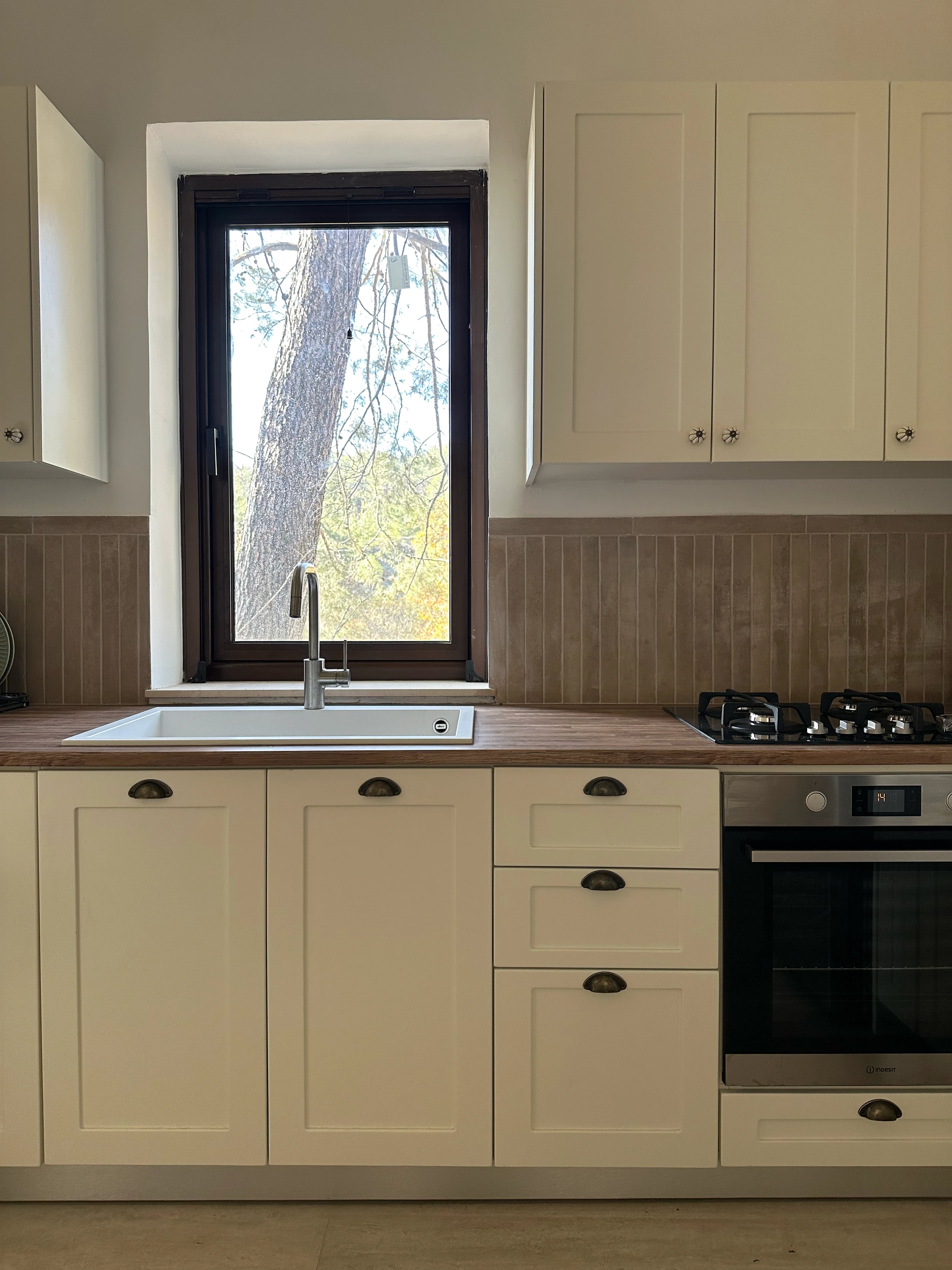 A cream kitchen with timber worktops, a white sink and a narrow window above the tap.