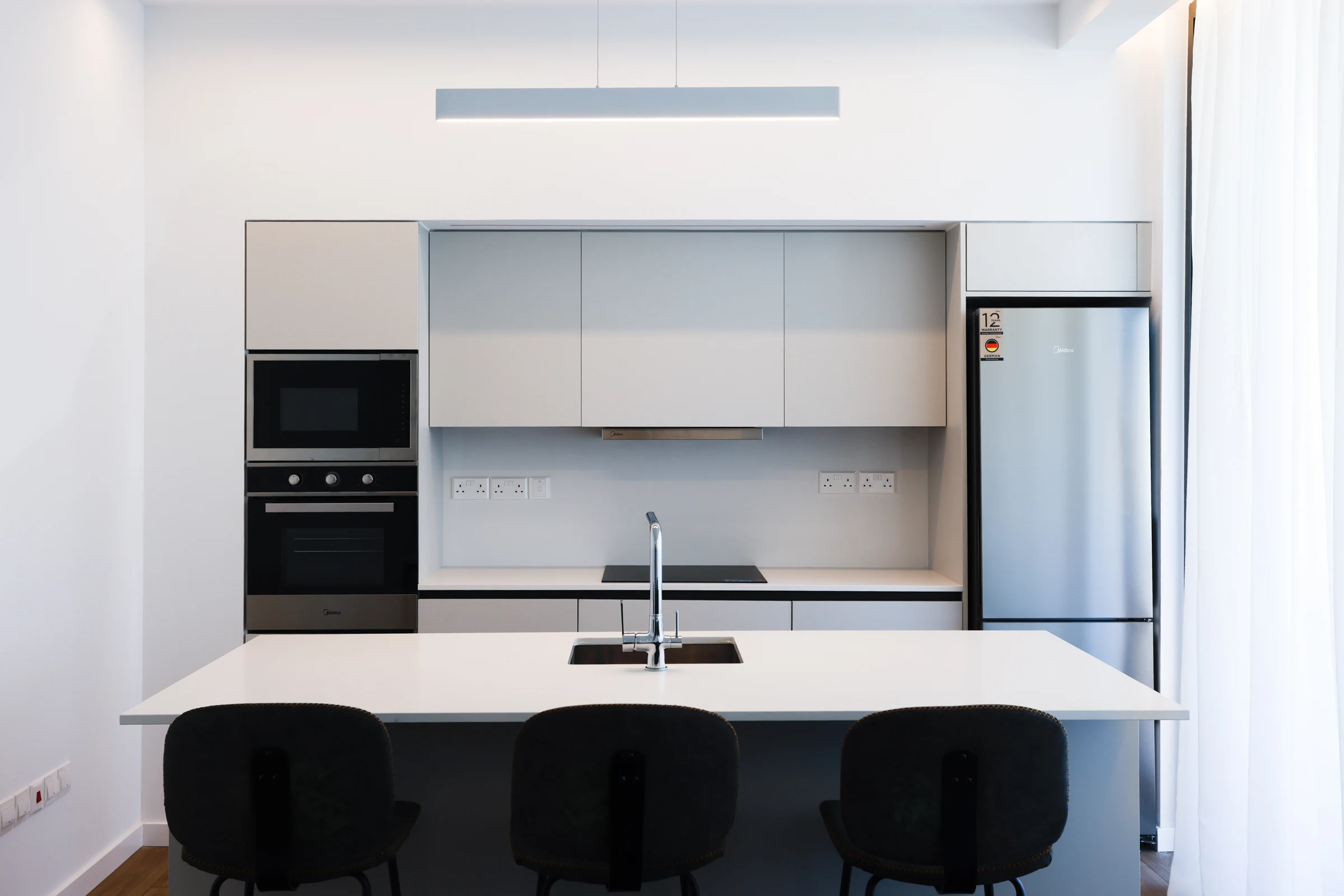A pale kitchen with a white island, three dark stools and tall integrated cabinetry.