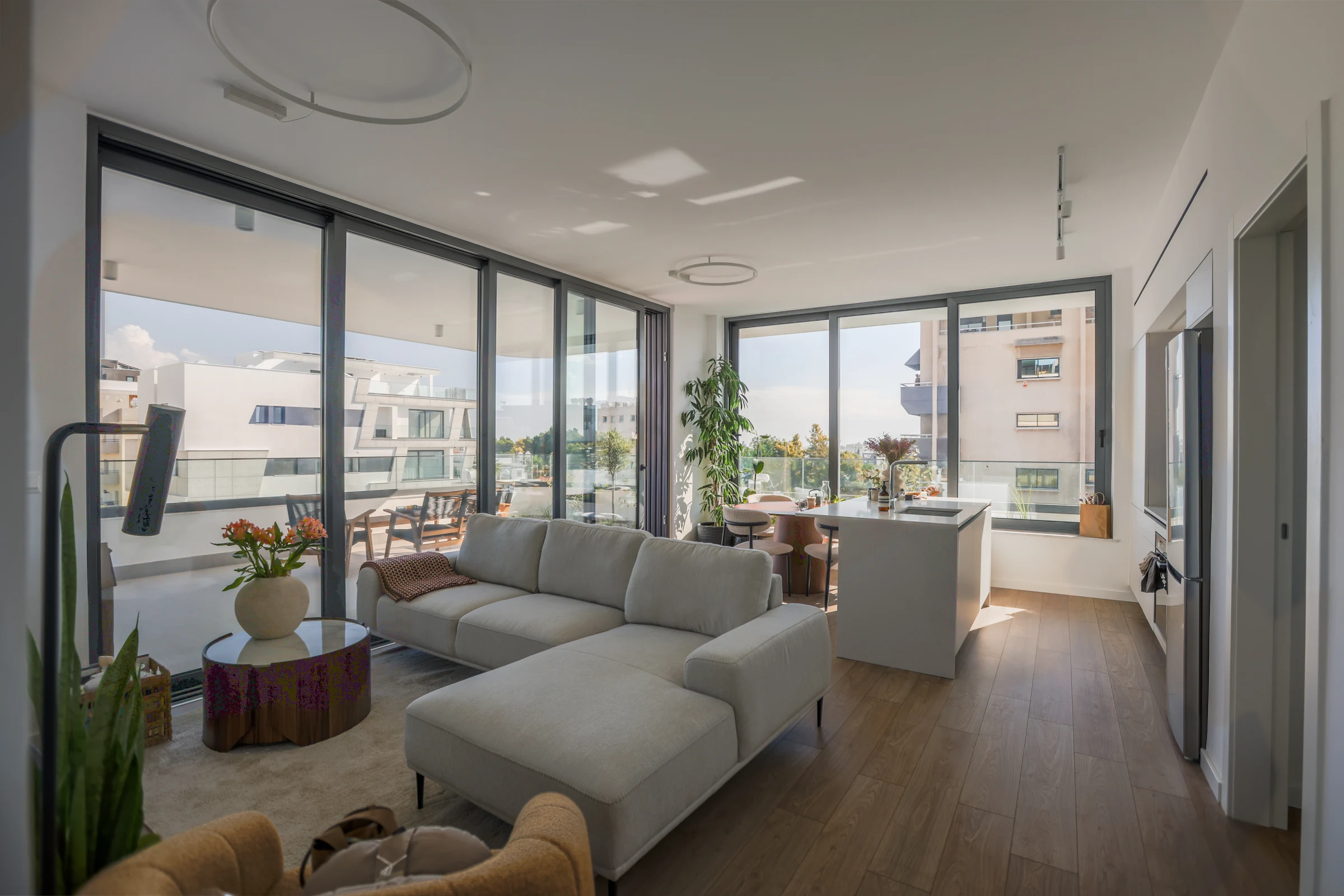 An open-plan living and dining room with a pale corner sofa and large windows opening toward a terrace.