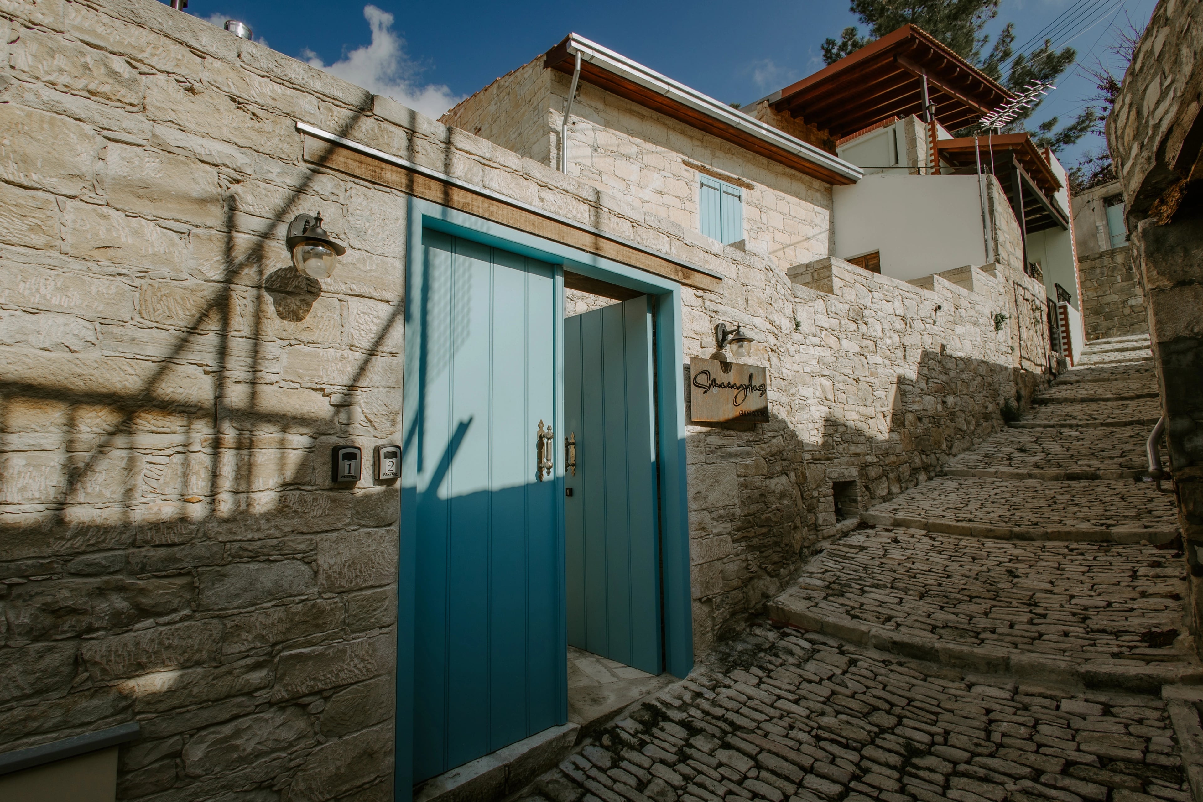 A stone village house with a turquoise entrance door beside a stepped cobbled lane.