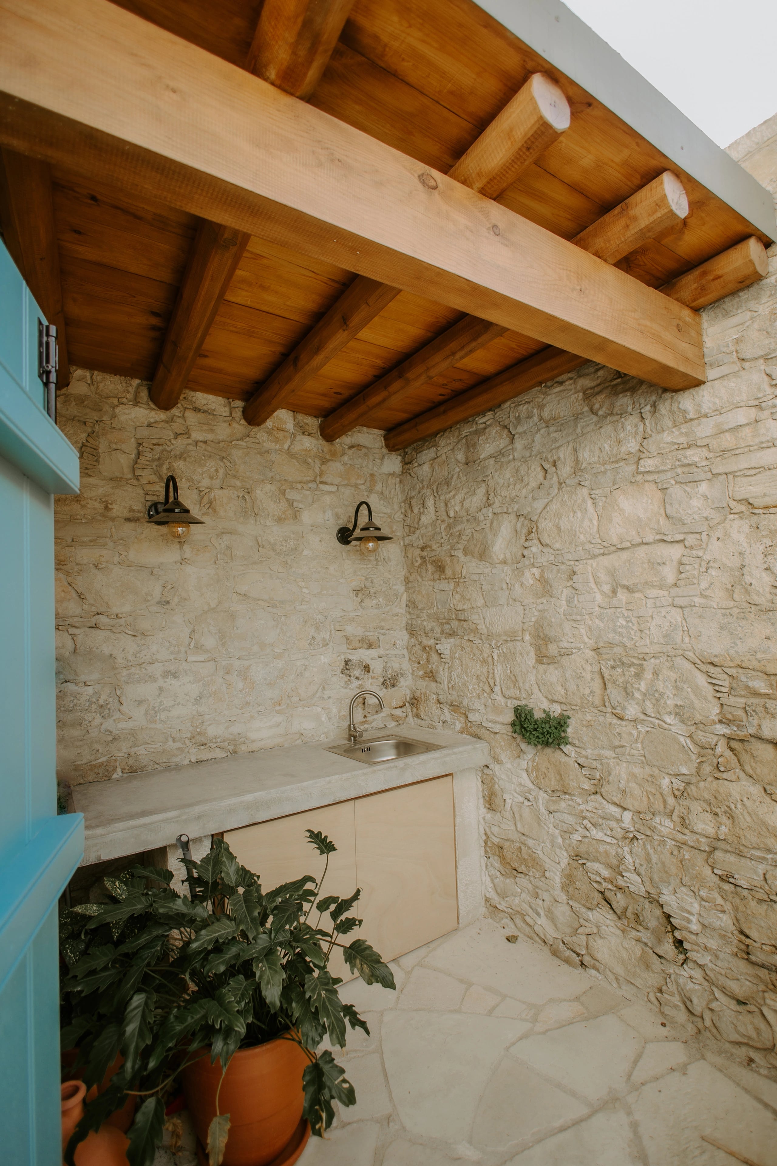 Exposed timber ceiling beams above a pale stone wall and a potted plant.