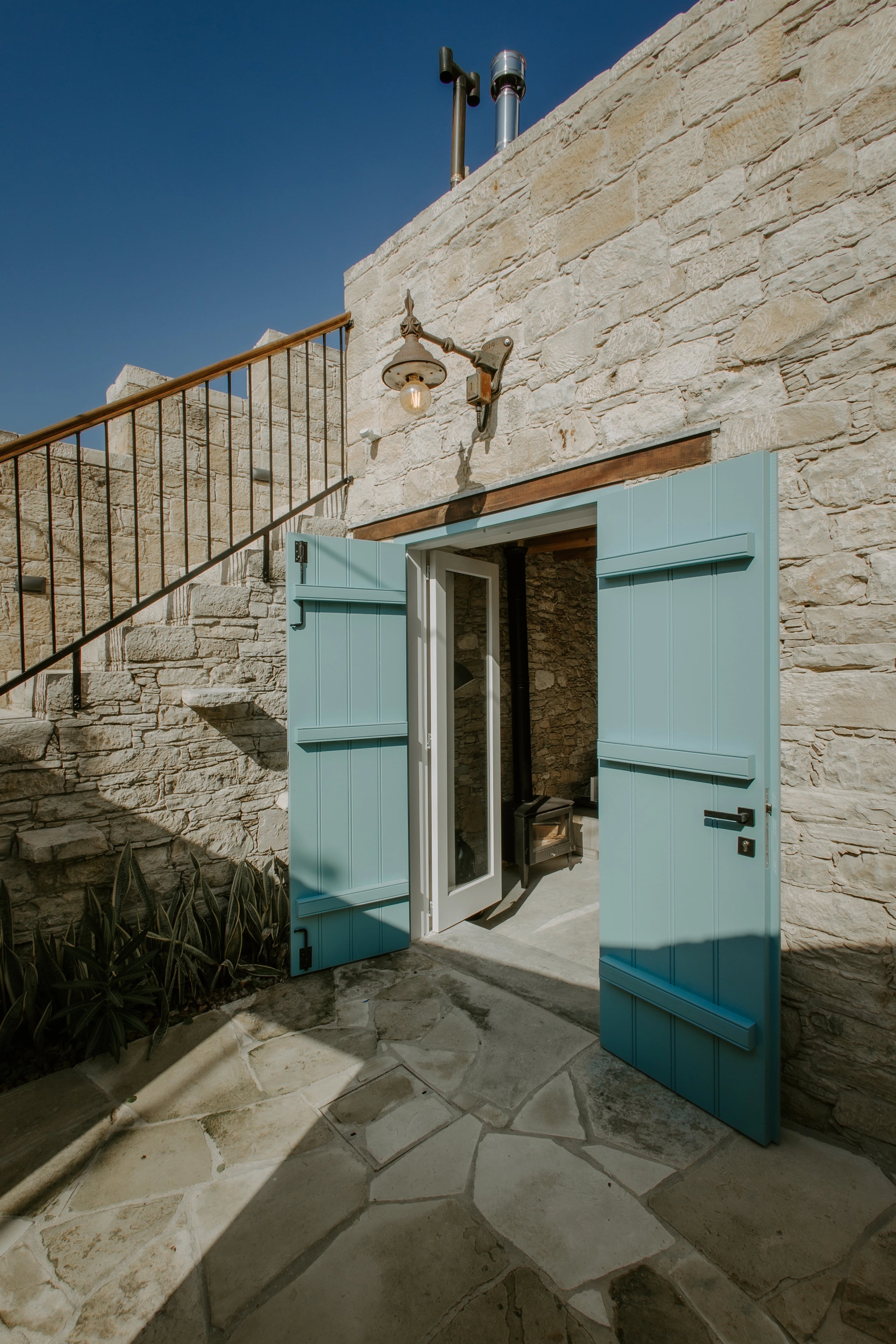 Open turquoise shutters in a stone courtyard beneath a timber balcony railing.