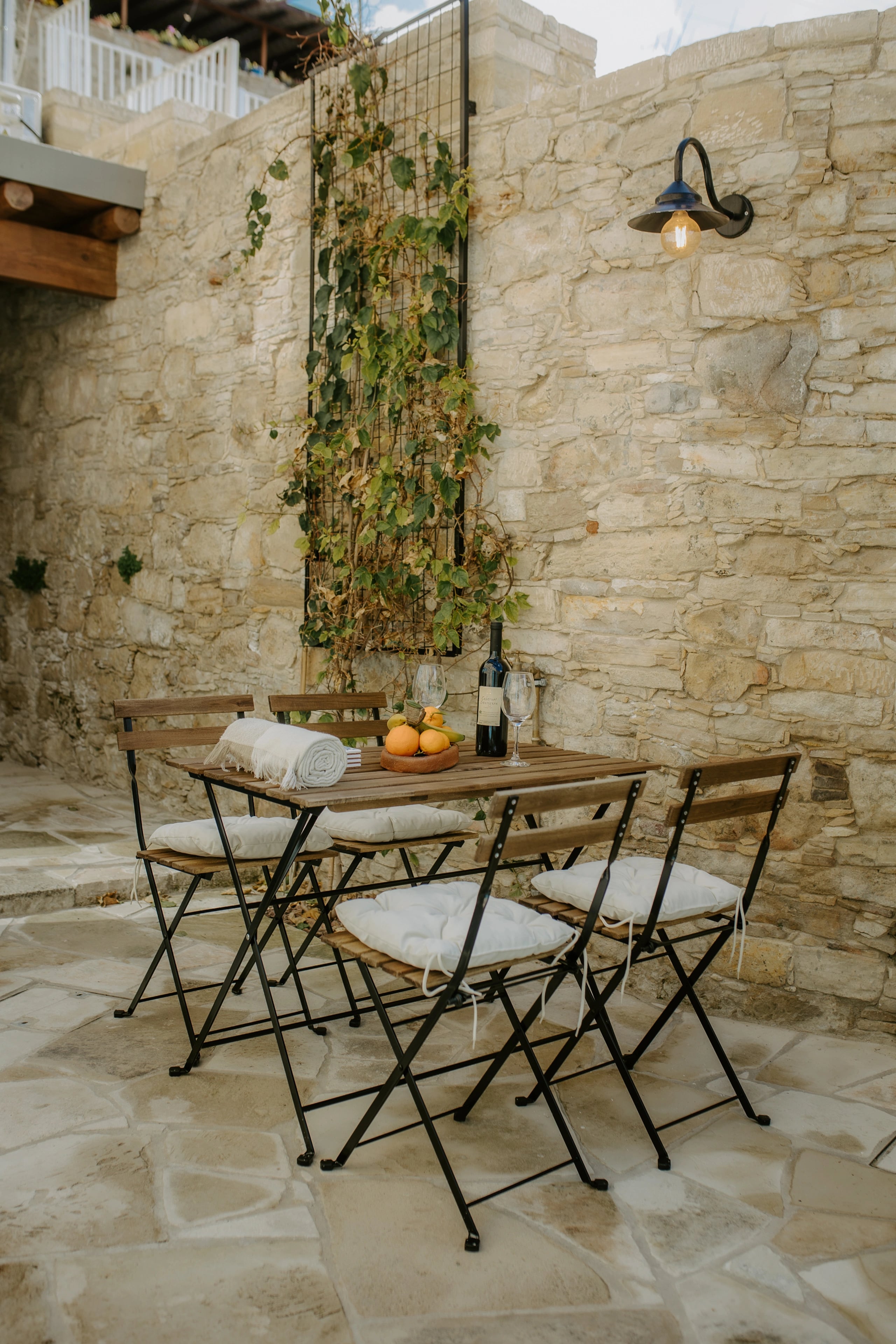 A small outdoor dining table and folding chairs in a sunlit stone courtyard.