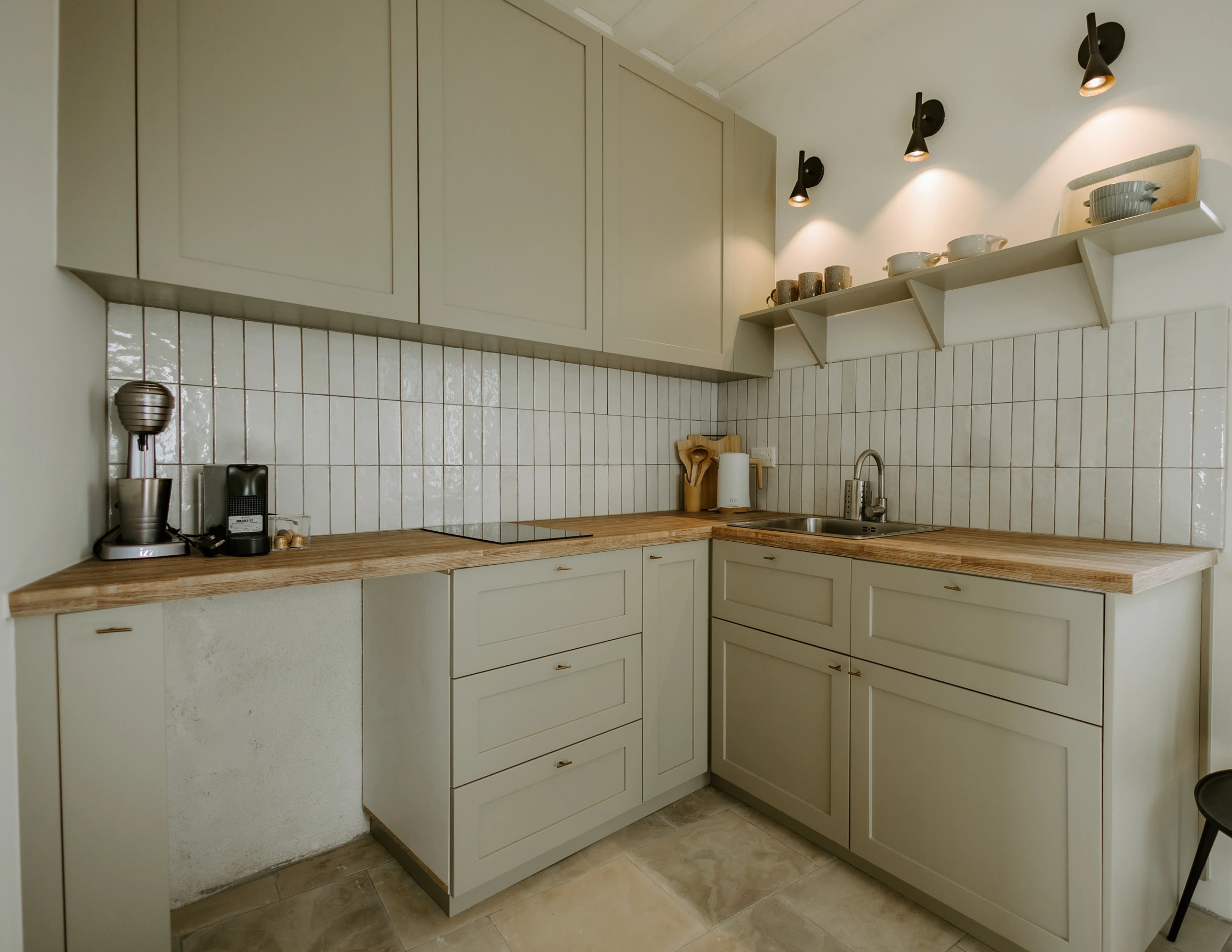 A pale-green corner kitchen with timber worktops, vertical tiles and wall-mounted lights.